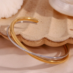 Close-up of dual-tone gold and silver crossover open cuff bracelet on shell tray