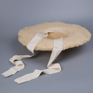 Close-up of a straw sun hat with frayed brim edges and long fabric ribbon ties