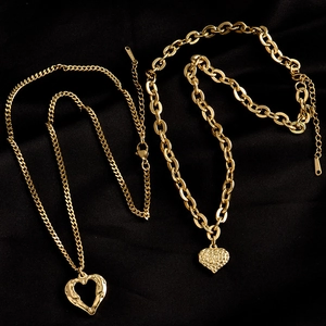 Set of two gold heart pendant necklaces featuring curb and cable chains on black background
