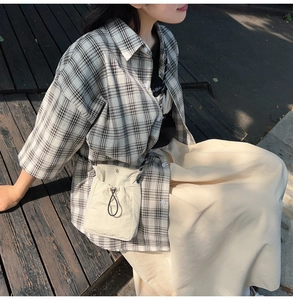 Close-up of beige canvas drawstring bag styled with a plaid shirt and beige long skirt