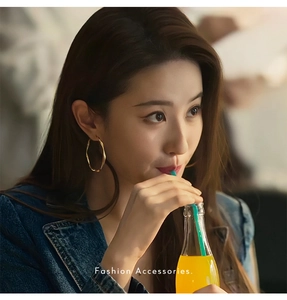Detail of twisted gold rope hoop earrings worn by a model in a casual denim jacket