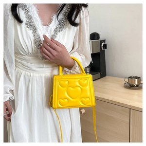 Détail du sac bandoulière jaune carré avec motifs de cœurs en relief sur cuir synthétique