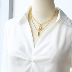 Détail du collier double rang plaqué or avec pendentifs cadenas et corne sur un mannequin