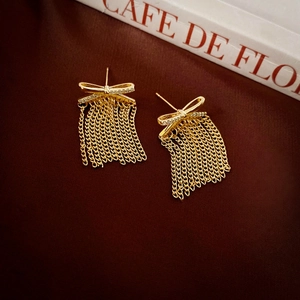 Elegant gold bow earrings with zircon tassels and silver needle on red velvet background