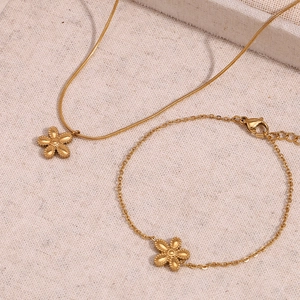 Detailed close-up of 18K gold plated flower necklace and matching bracelet on linen texture