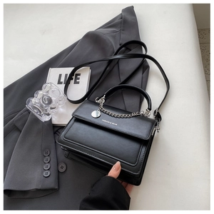 Detail of black crossbody bag featuring silver chain decor and textured faux leather finish
