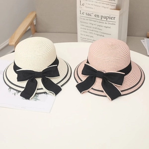 Dettaglio ravvicinato di cappelli di paglia estivi color crema e rosa con eleganti fiocchi neri