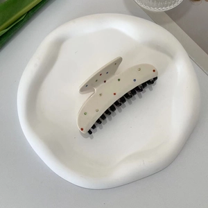 Detail of beige acetate hair claw clip with colorful rhinestones on a white plate