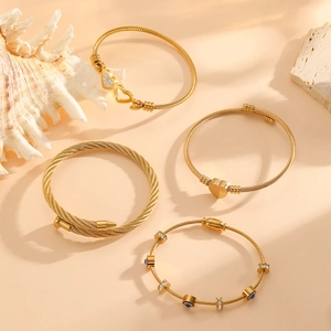 Détail de quatre bracelets câbles en acier inoxydable doré avec charms cœur et œil