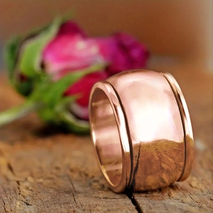 Macro shot of wide polished copper ring with groove edges on a wooden surface