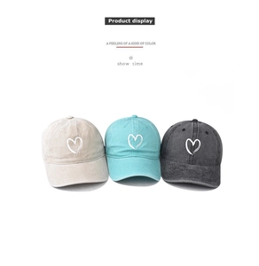 Detail of heart embroidery on washed cotton baseball caps in beige green and grey