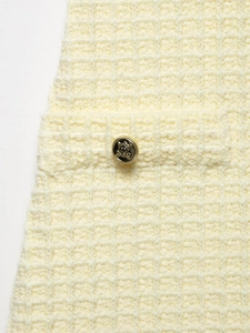 Vista detallada de la textura del tejido tweed crema y botón dorado de escudo