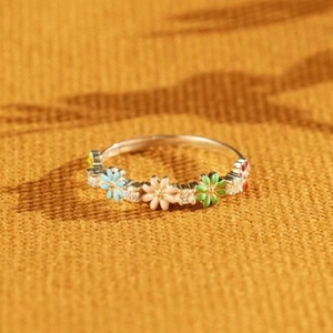 Detail of colorful floral enamel ring with crystal accents on a textured yellow background