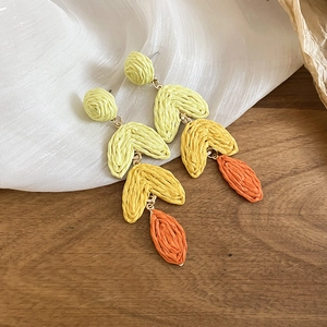 Detail of woven raffia tassel earrings with green, yellow, and orange gradient fringe