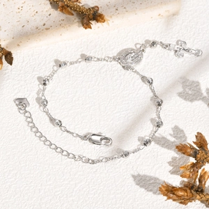 Détail du bracelet en perles argentées avec médaille de la Vierge et pendentif croix