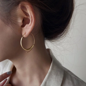 Profile view of a model wearing large matte gold hoop earrings with a modern thick design