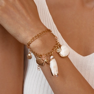 Close-up of bohemian gold chain bracelet with sea shells and starfish charms on wrist