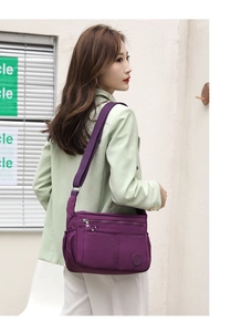 Vista detallada de un bolso bandolera de nailon morado con múltiples bolsillos en una modelo