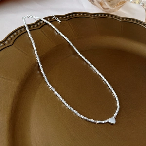 Silver necklace with irregular beads and heart pendant on a vintage tray detail