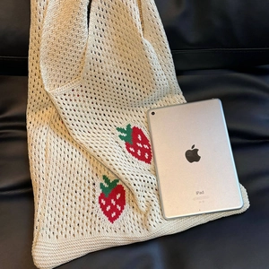 Detailed view of cream knit tote bag with strawberry pattern holding a large tablet