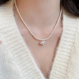 Close-up of a pearl necklace with a colorful rocking horse pendant on a female model