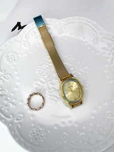 Detail view of a vintage gold quartz watch with mesh strap and hollow ring on ceramic tray