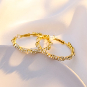 Macro shot of gold hoop earrings with sparkling white zircon insets on silk fabric