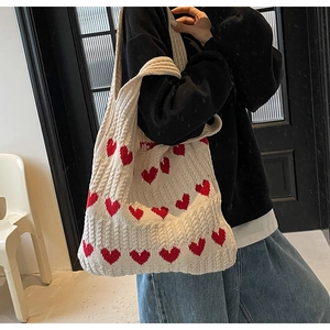 Mujer lleva un bolso de punto crema con corazones rojos en un ambiente de interior