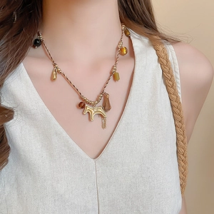 Detail of woven rope necklace with a golden horse pendant and flowing metal tassels