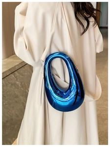 Blue metallic oval drop bag with silver chain strap worn by a model in beige coat