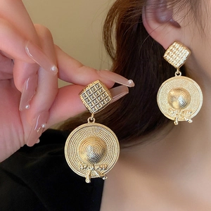 Detail of vintage gold-tone earrings with textured square and hat-shaped design on model