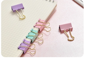Close-up of pastel macaron binder clips on a pink desk and grid notebook