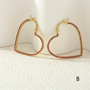 Detailed macro view of gold-tone heart hoop earrings with pavé set red crystals