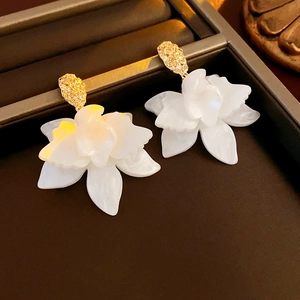 Detailed close-up of white 3D resin flower earrings with gold metal base on jewelry tray