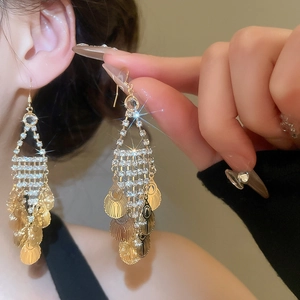 Macro shot of elegant gold tassel earrings with shimmering crystals and leaf-shaped metal scales