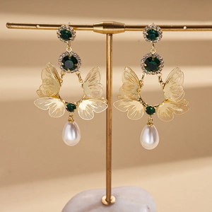 Detailed close-up of butterfly earrings with green stones and pearl drop pendants