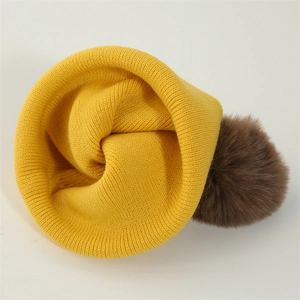 Detailed top view of a yellow knitted baby hat featuring a fluffy brown pom-pom decoration