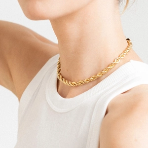 Gros plan d'un collier chaîne torsadée dorée porté par un mannequin au style minimaliste