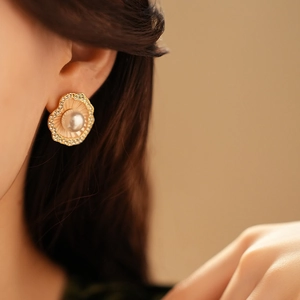 Gros plan d'une boucle d'oreille dorée en perle avec design feuille de coquillage sur modèle