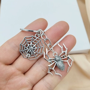Detail of silver spider and web charms on a metal keychain held in hand closeup
