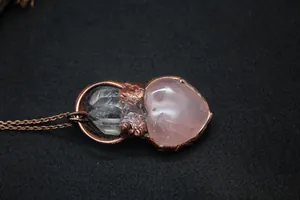 Macro detail of a heart-shaped pink quartz pendant with raw crystal clusters on copper chain