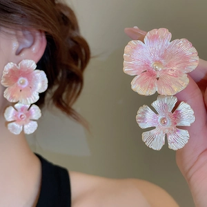 Close-up of pink flower earrings with metallic texture worn on a model's ear