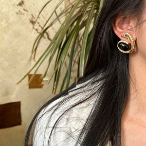 Detail view of retro gold spiral earrings with oval black resin stone on female model