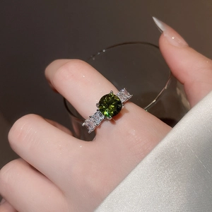 Close-up of a silver ring with a green emerald gemstone and baguette diamonds on a finger
