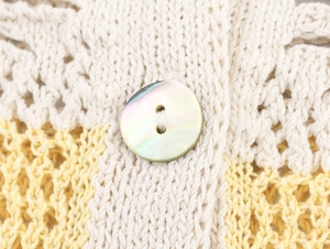 Macro shot of iridescent shell button on yellow and beige crochet knit textured top