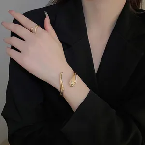 Minimalist gold snake-shaped open bracelet and ring set worn on a black sleeve