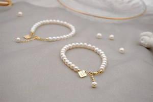 Detail of freshwater pearl bracelets with gold Good Luck pendants on silk background