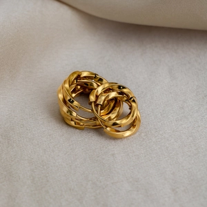 Detailed close-up of golden twisted hoop earrings on soft beige linen fabric texture