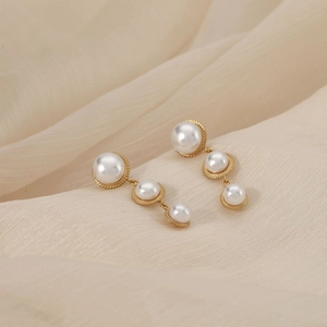 Elegant gold earrings featuring three graduated white pearls on a soft silk background