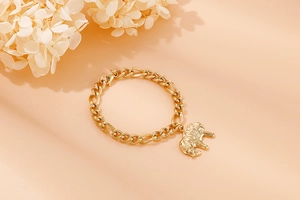 Detail view of a gold-tone chunky chain bracelet with elephant charm on peach background